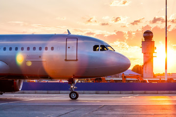 Obraz premium Zbliżenie przodu samolotu pasażerskiego. Samoloty kołujące na płycie postojowej lotniska w promieniach malowniczego wschodu słońca