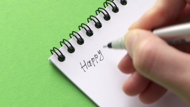 Write Happy St. Patrick's Day on white notepad paper. Female hand leave note or letter on green background, close-up