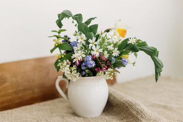 Countryside bouquet. Spring wildflowers in vintage cup on rustic wooden table. Blooming colorful flowers of ajuga, forget-me-nots, daffodils, pulmonaria, rabelera holostea and greenery.