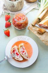 Tasty strawberry rhubarb strudel cake with sweet berries sauce in plate with fork on light table background with ingredients. Top view. Organic home baking. Seasonal eating