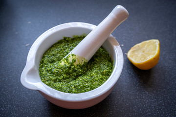 Making wild garlic pesto by grinding wild garlic leaves with olive oil, pine nuts, hazelnuts, lemon juice and olive oil in a mort and pestle