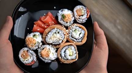 homemade asian style sushi rolls. philadelphia and california rolls on a black plate with marinated ginger. human hands holding oriental appetizer.