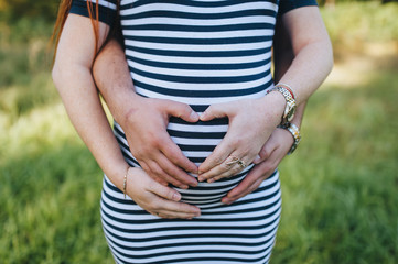 A pregnant woman and a man hold on to their stomach and show their hands with their heart. Expectation of a child from parents. Photography, concept.