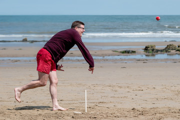 A man on the beach playing cricket, bowling the ball in front of the sea