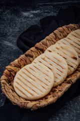 Top view of woven basket filled with a group of Latin American arepas on a dark background