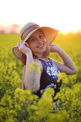 Beautiful girl in a straw hat walks in a field at sunset