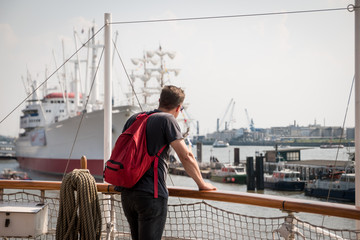 Fototapeta premium A tourist stands on a ship deck overlooking the harbour and other boats in the port