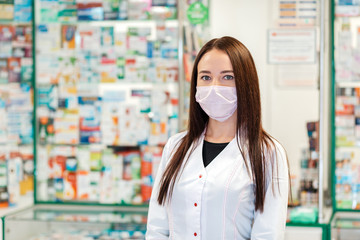 A female pharmacist in a medical mask poses against the background of a pharmacy window in a blur....