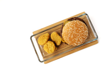 Cheeseburger, nuggets in the glass plate. Bamboo board. White background. Isolated objects.