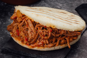 Arepa stuffed with shredded meat on a dark background. (Arepa con carne mechada)