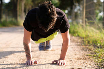 Social distancing - Caucasian man doing push-ups outside to maintain good mental health, wearing a black t-shirt and green shorts and with tattoos in his arms