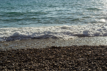 pebble stones on the sea beach, the rolling waves of the sea with foam