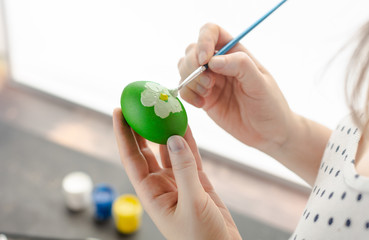 Woman painting with watercolors on egg to prepare Easter eggs.