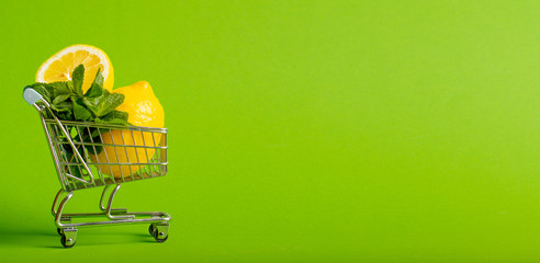 Lemons and mint in a small toy cart on a green background. online shop delivery concept. you can use it as banner with your text