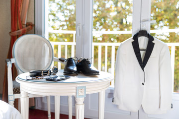 Table à thé, avec les accessoires, chaussures, montre du marié et sa veste devant un fenetre - obrazy, fototapety, plakaty