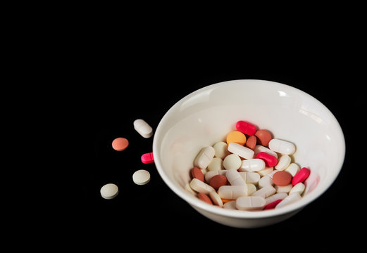 Different medicine pills, tablets in a white saucer on black background. Many different pills. Health care. Top view. Space for text. Copy space. New image. Closeup. Pharmaceutical picture