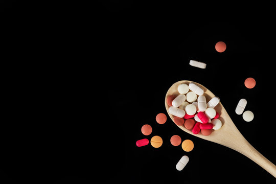 Different medicine pills, tablets on wooden spoon on black background. Many different pills. Health care. Top view. Space for text. Copy space. New image. Closeup. Flatlay. Pharmaceutical picture