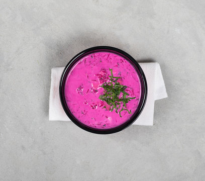 Cold beetroot soup with parsley in a bowl on a light gray background top view