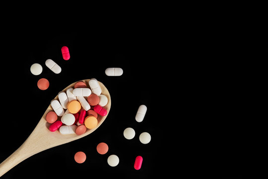 Mixed medicine pills, tablets on wooden spoon on dark background. Many different pills and capsules. Health care. Top view. Space for text. Copy space. New image. Pharmaceutical picture. Nice flatlay