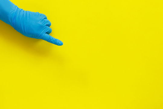 Hand In Medical Glove Pointing Finger On Yellow Paper Background