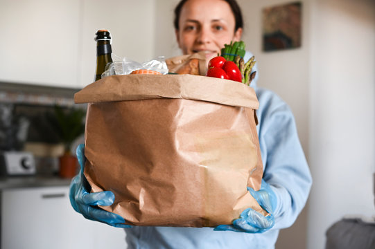 A person smiling for the camera with a set of food in hand.. Paper bag with Food supplies crisis food stock for quarantine isolation period. Food delivery, Donation, coronavirus. Soft focus