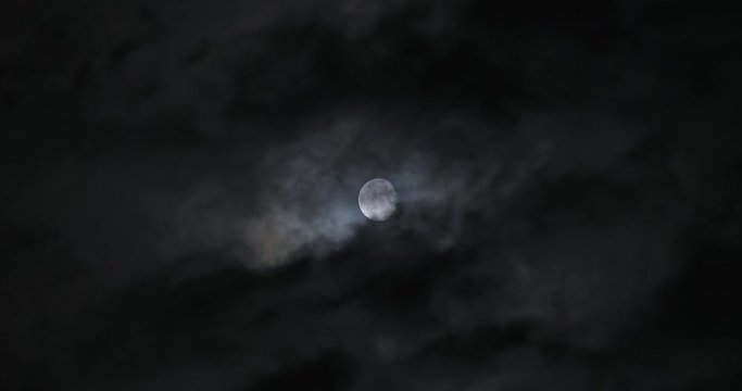 Moon shot behind dark clouds moving at night in real time
