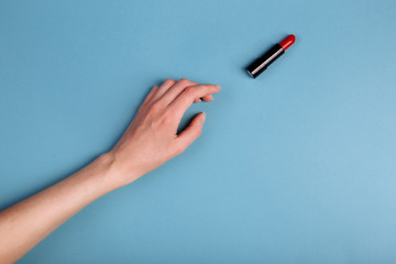 The woman's hand is taking red lipstick. isolated On the blue background