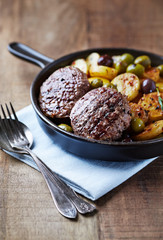 Grilled hamburger steaks with potatoes and olives. Rustic wooden background.