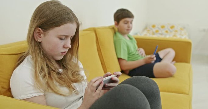 Two kids with gadgets. Sister and brother surfing the net or playing online games on smartphone and digital tablet at home. Modern communication and gadget addiction concept