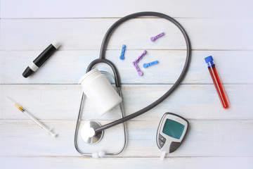 blood glucose meter, medical device for measuring blood glucose, laboratory test tube with blood, empty white jar for drugs and a stethoscope, health concept, patient monitoring