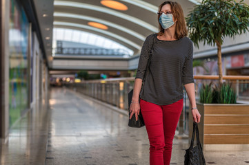 Junge Frau mit Atemschutzmaske läuft durch ein leeres Einkaufszentrum