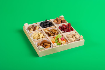 Assorted dried fruits and nuts in a wooden box isolated on a green background. Raisins, candied fruits, cherries, Brazil nuts, hazelnuts, walnuts, almonds, cashews, pistachios.