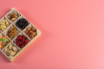 Assorted dried fruits and nuts in a wooden box isolated on a pink background. Raisins, candied fruits, cherries, Brazil nuts, hazelnuts, walnuts, almonds, cashews, pistachios.