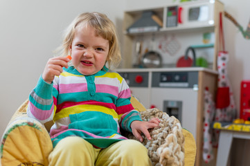 Cute blonde girl sitting in a children couch making faces at home.