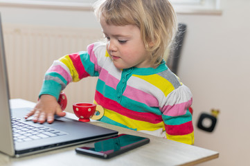 Naklejka premium Cute blonde girl having a drink while working on a computer.