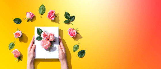 Female hands holding a gift box with pink roses overhead view - flat lay