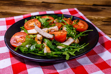 Roasted chicken breasts and salad with arugula and cherry tomatoes in a black plate