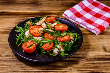 Roasted chicken breasts and salad with arugula and cherry tomatoes in a black plate