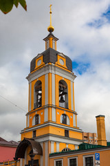 Obraz premium Tall yellow bell tower of an Orthodox church with a golden dome against a cloudy sky
