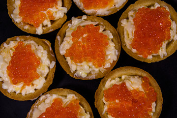 Tartlets with red caviar on a black plate. Festive food. Top view