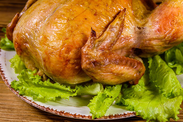 Plate with roasted whole chicken and lettuce leaves on a wooden table