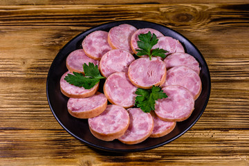 Black plate with sliced sausage on a wooden table