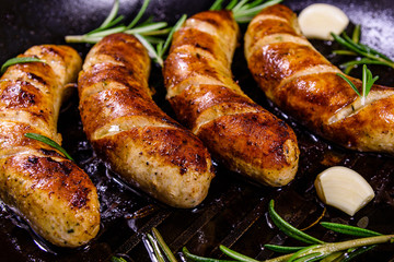 Roasted sausages with rosemary twigs and garlic in a cast iron grill pan