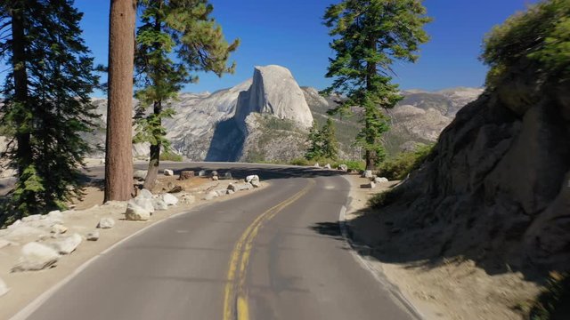 Aerial following the picturesque mountainous automobile road towards the fantastic view of the famous symbol of Yosemite National Park, the Half Dome rock and the beautiful Sierra Nevada range. 4K