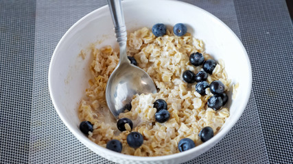 man eats delicious oatmeal cereals with blueberries and milk for breakfast at home close-up