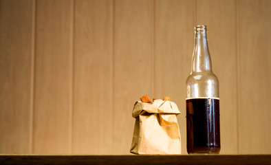 Bottle of beer and a paper bag with crackers on the table.