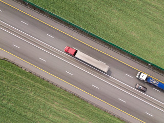 Dump trucks carrying goods on the highway. Red truck driving on asphalt road along the green...
