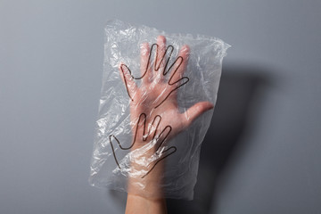 Woman's hand in disposable plastic protective gloves on gray background, close-up shot, Prevention...