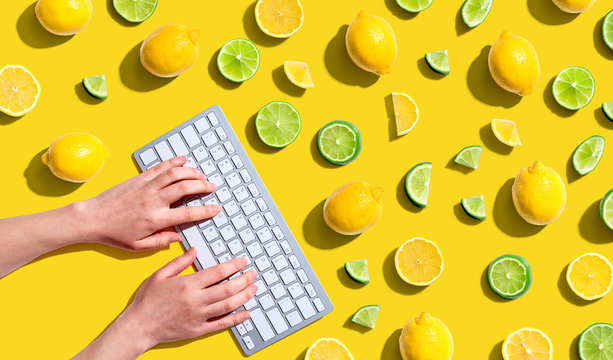 Woman using a computer keyboard with fresh lemons and limes overhead view - flat lay