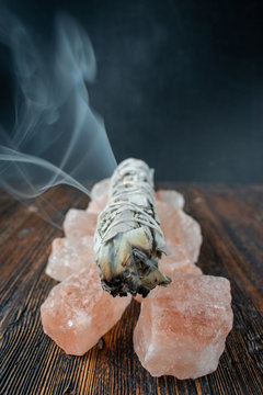 burning a smudge sage stick on a base of pink salt crystals with smoke trail
